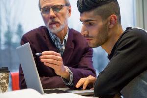 Older man working with younger man on computer.