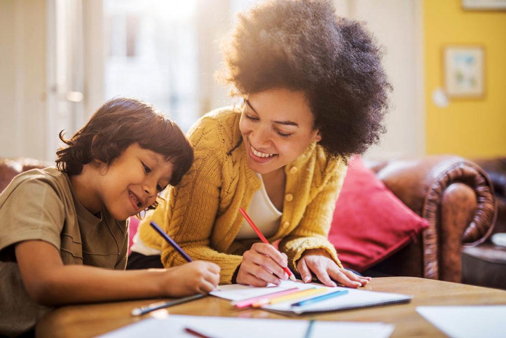 Young happy mother having fun with her son at home while coloring together.